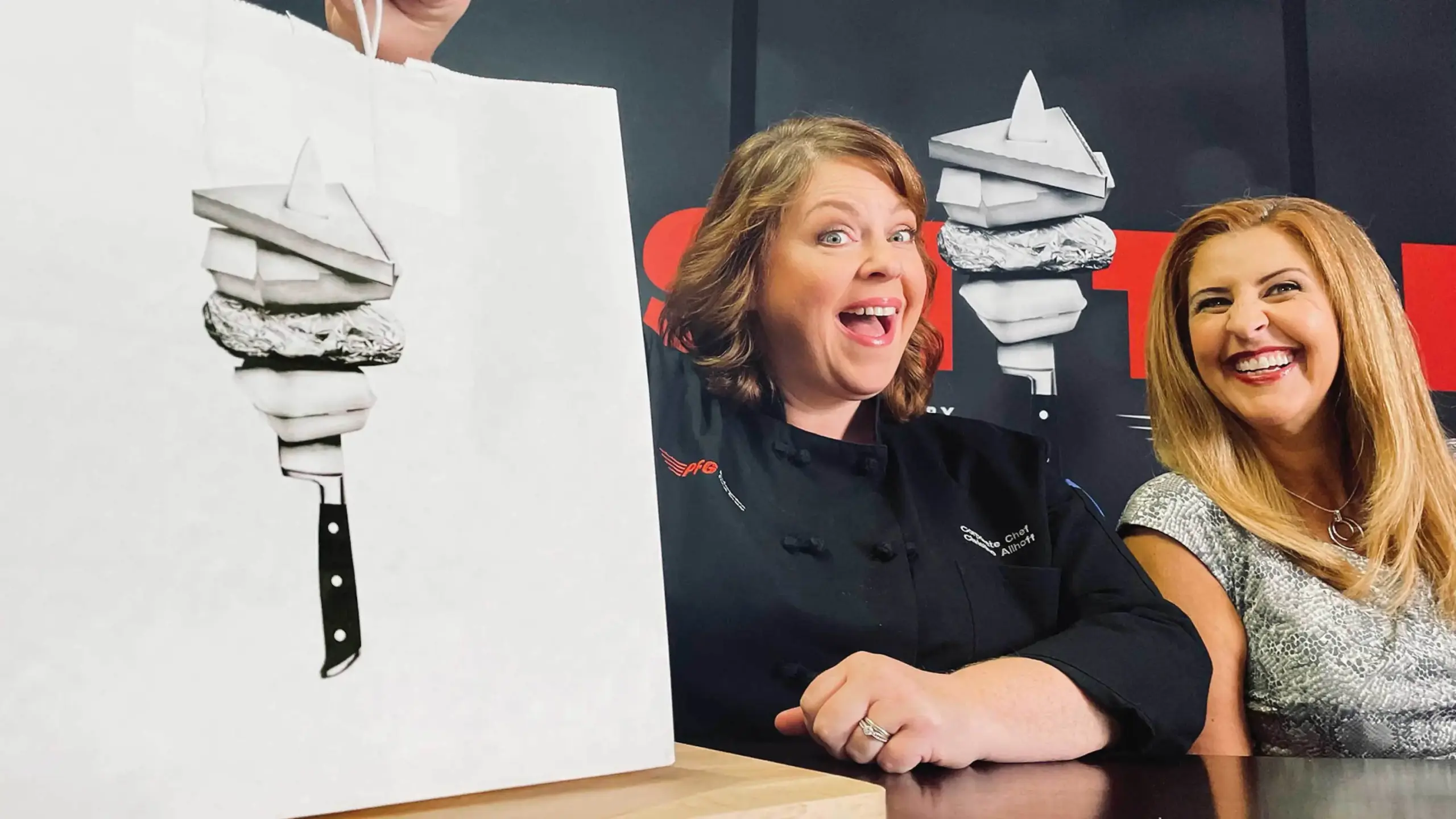 Chef Christine and Sharon smiling in front of the backdrop with FreshTakes by Performance Food Group branding