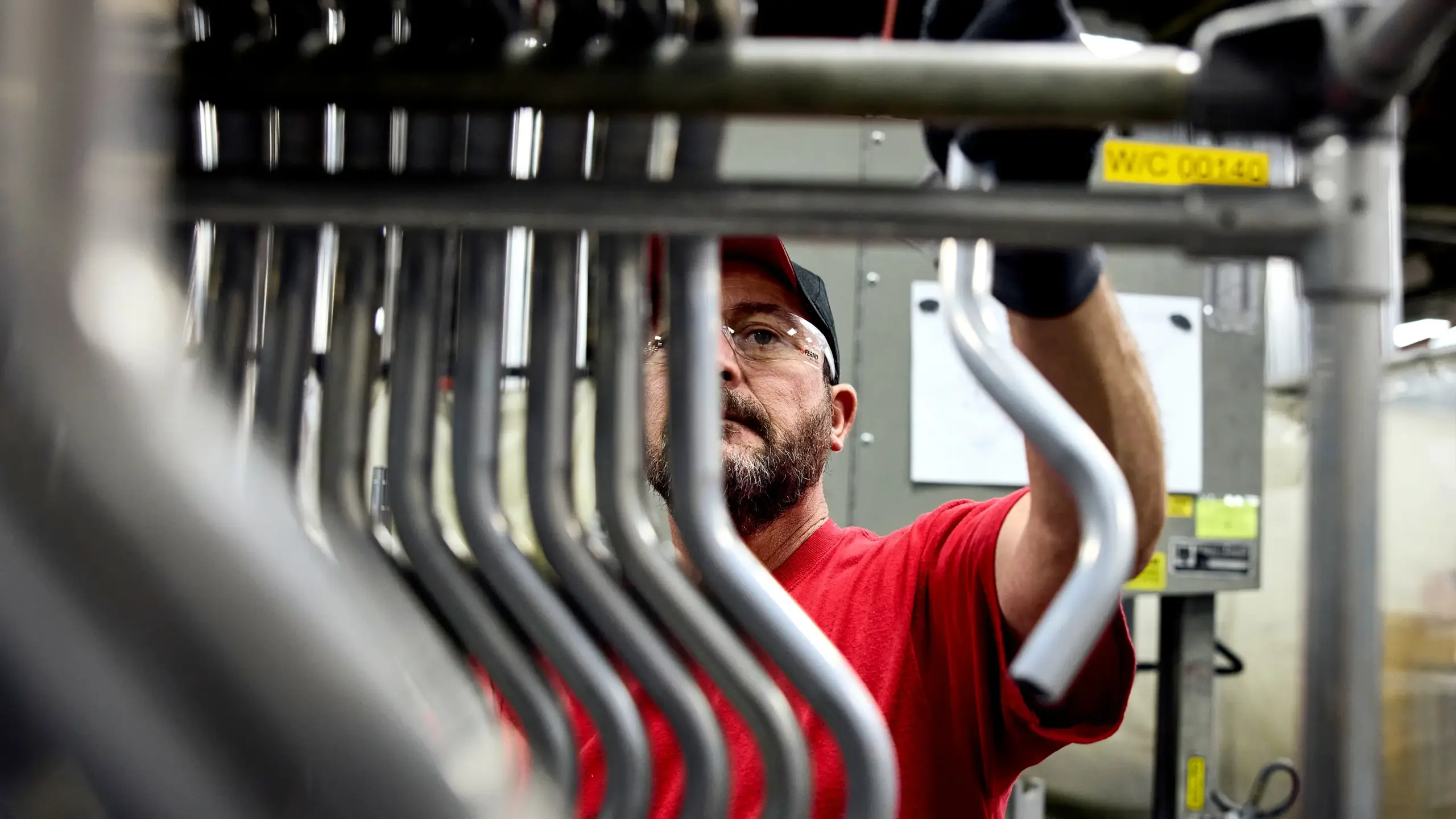 Factory worker inspecting and assembling metal components on industrial equipment during EMS product manufacturing