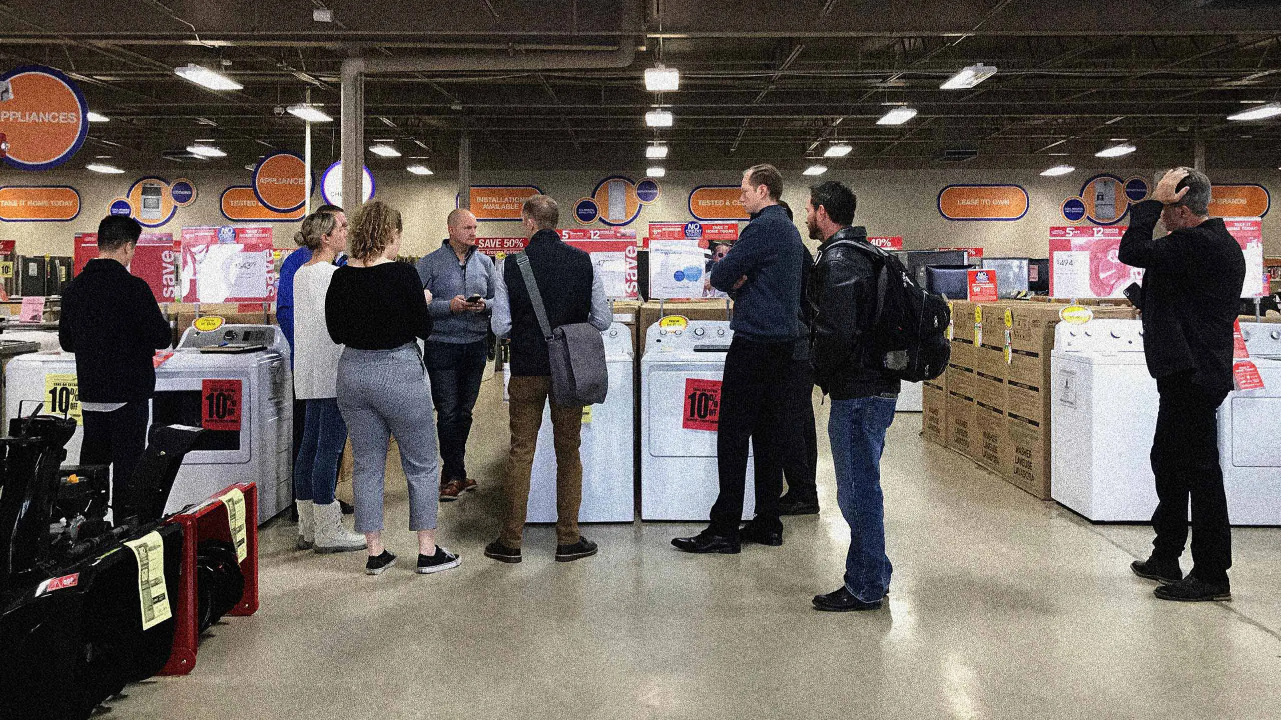 The Multiple team members walking through an entryway with a Sears Outlet sign next to appliances