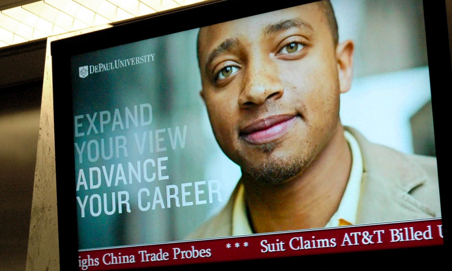 A confident man in business attire appears in a DePaul University ad on a screen, promoting career advancement.