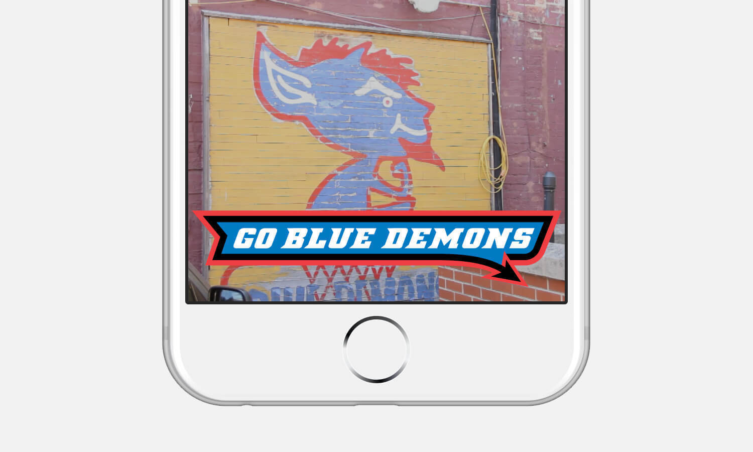 Mural featuring a blue and red cartoon demon on a brick wall behind a "Go Blue Demons" banner on a smartphone screen.