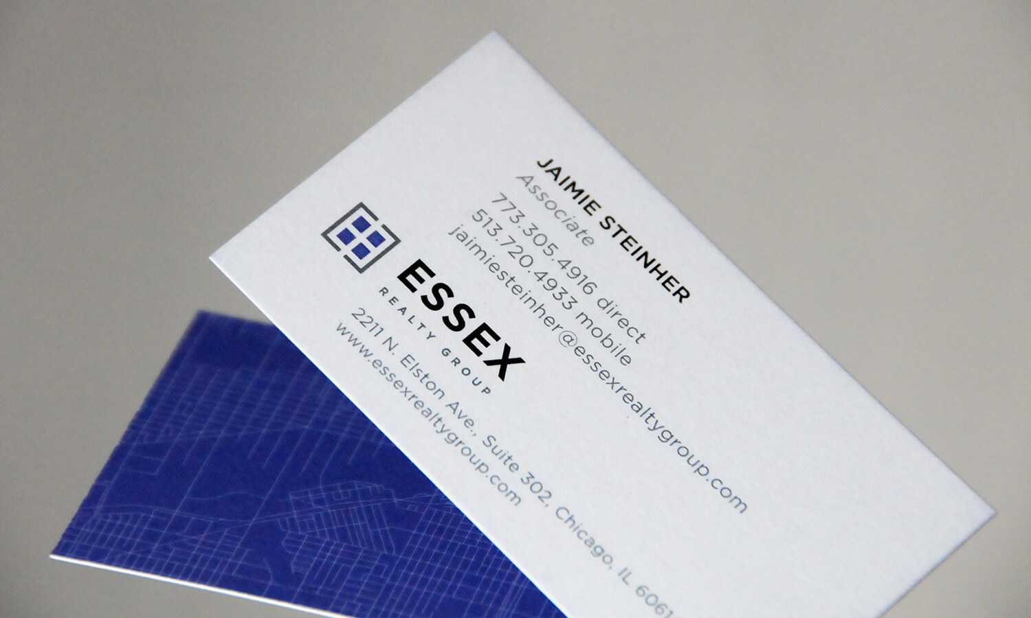 A business card for Essex Realty Group showing contact details with a modern blue geometric logo with subtle blue map design on the back.