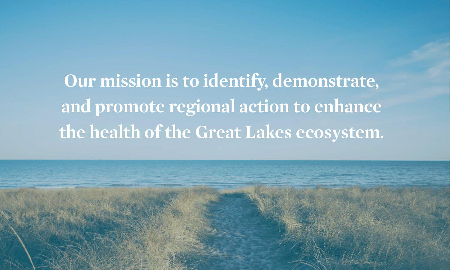 A serene beach scene with a path through dune grass leading to a calm lake under a clear blue sky. Text reads, "Our mission is to identify, demonstrate, and promote regional action to enhance the health of the Great Lakes ecosystem."